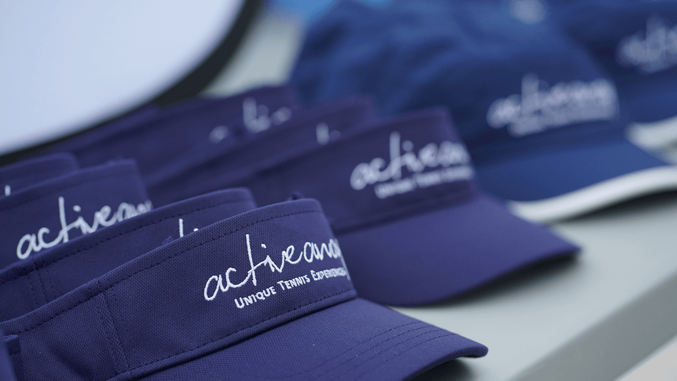 Close-up of navy Active Away tennis visors and caps with embroidered logo on a table.