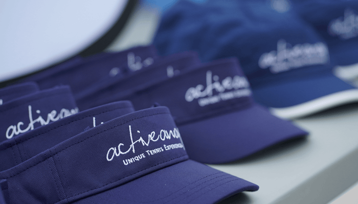 Close-up of navy Active Away tennis visors and caps with embroidered logo on a table.