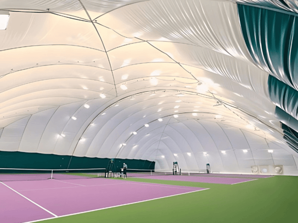 Indoor tennis courts beneath an air-supported dome with purple courts and green surrounds.