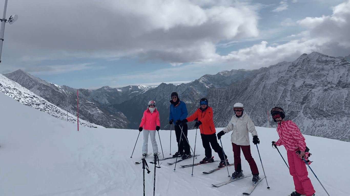 Group of skiers posing on a snowy slope with dramatic Alpine mountains in the background.