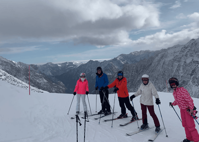 Group of skiers posing on a snowy slope with dramatic Alpine mountains in the background.