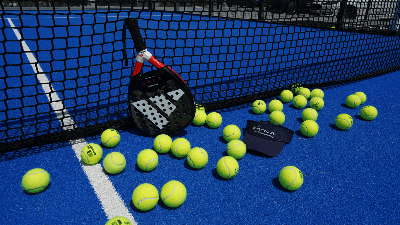 Padel racket and scattered tennis balls on a blue court beside a net, with an Active Away visor.