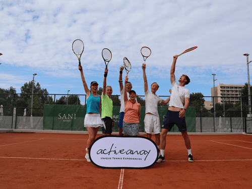 Group of adults celebrating on a clay tennis court, lifting racquets beside an Active Away sign at Sani Resort.