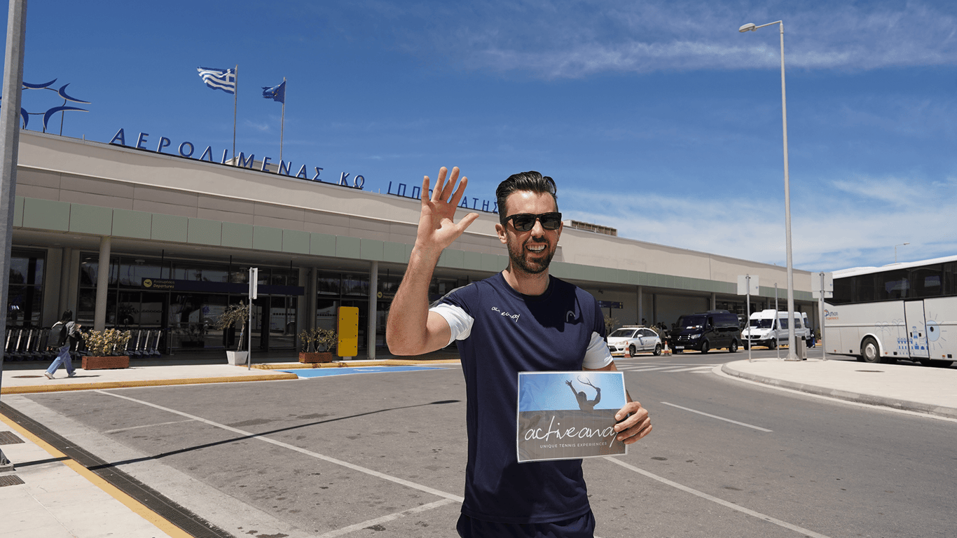 Smiling man holding an Active Away sign outside a Greek airport, ready to greet arriving guests.
