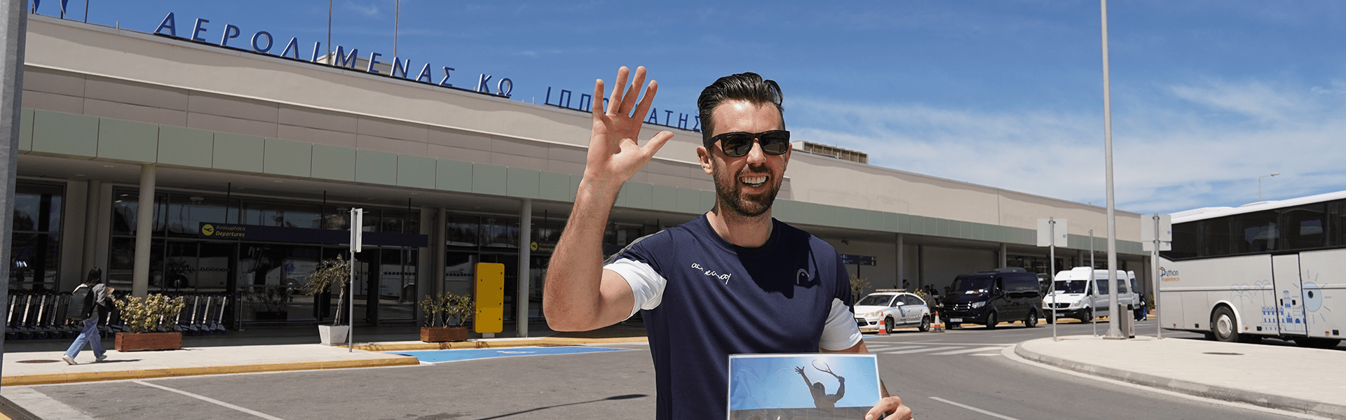 Smiling man holding an Active Away sign outside a Greek airport, ready to greet arriving guests.