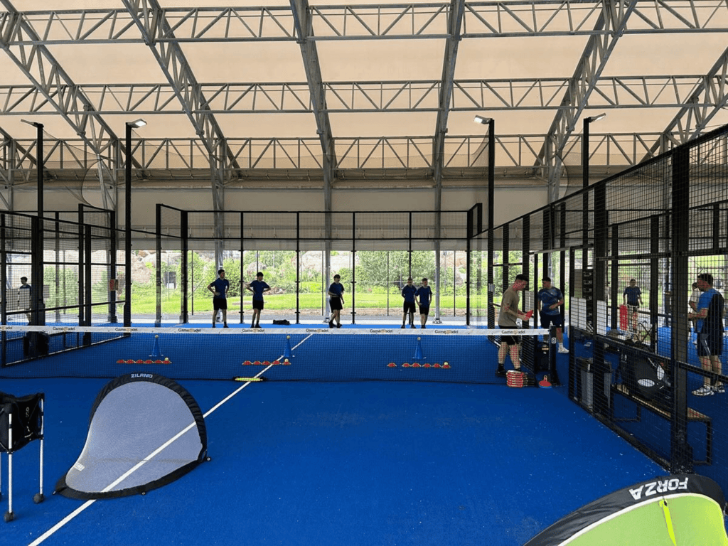 Players train on covered blue padel courts with cones and nets during a coaching session.