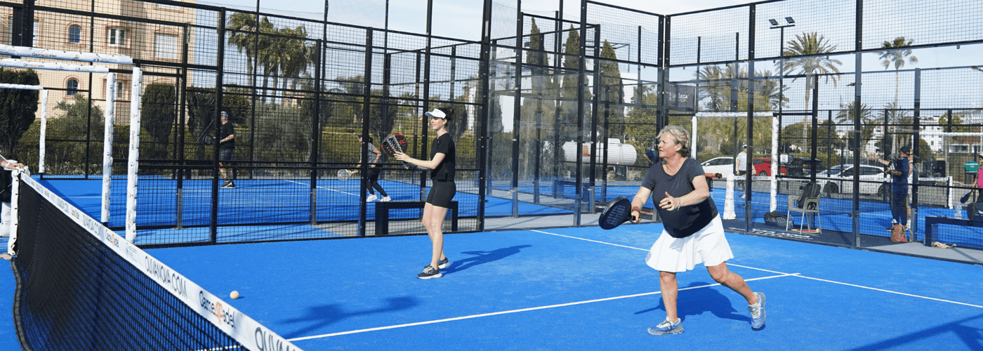 Active Away coach demonstrating a padel forehand on a blue outdoor court with players nearby.