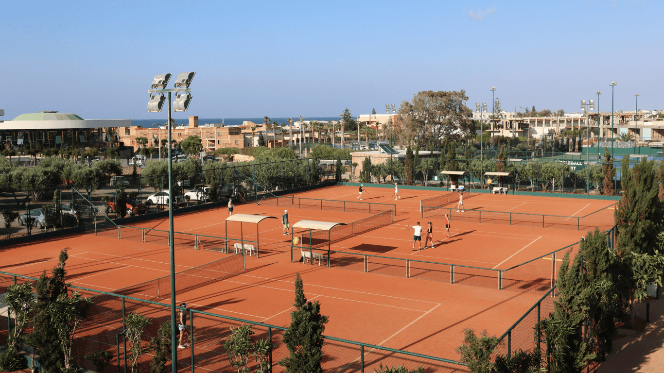 Coach leads serve drills on clay courts at a seaside resort.