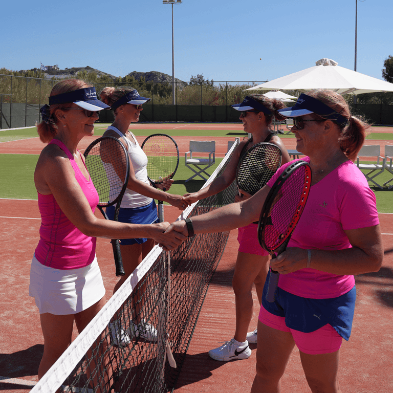 Four women shake hands at the net after a doubles match on a sunny tennis holiday.