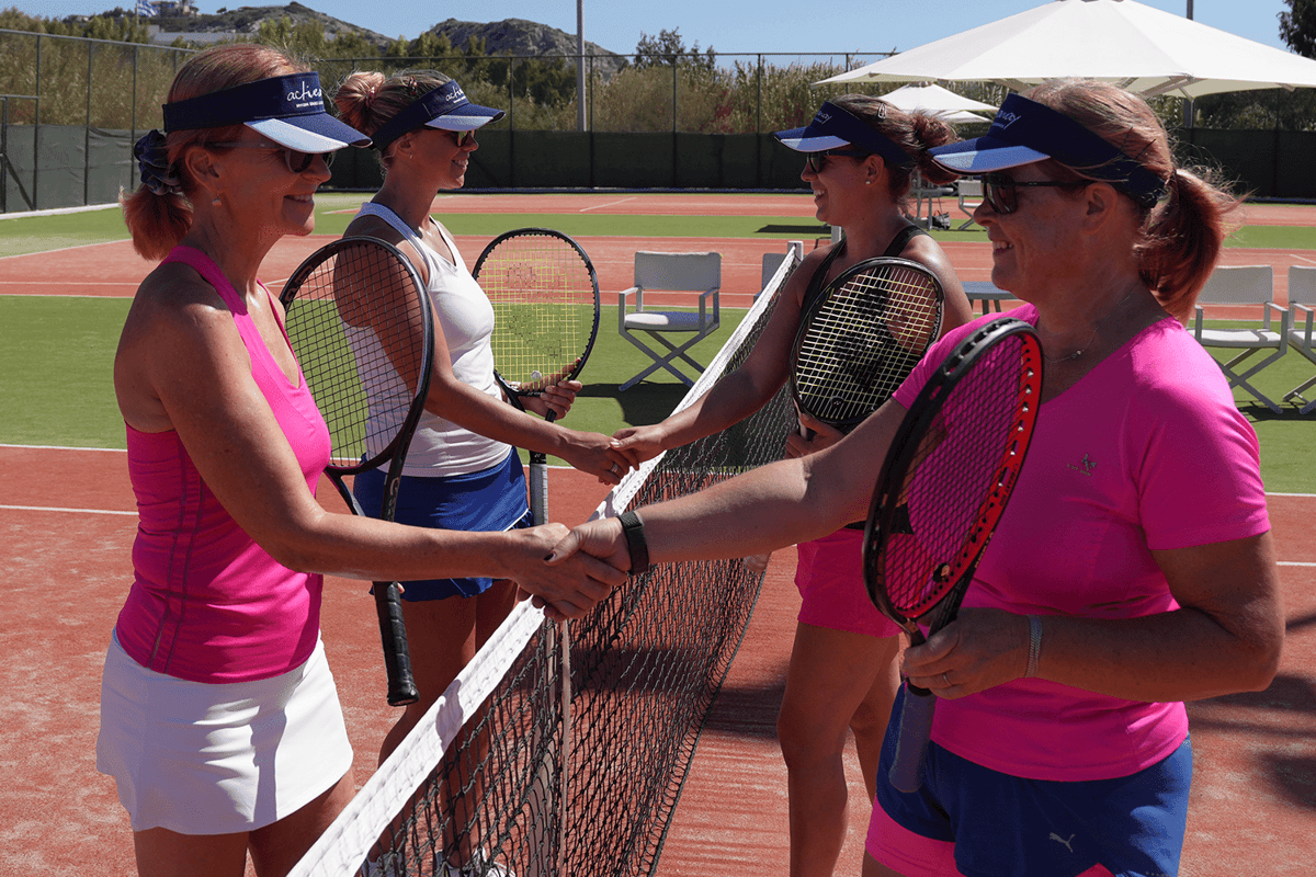 Four women shake hands at the net after a doubles match on a sunny tennis holiday.