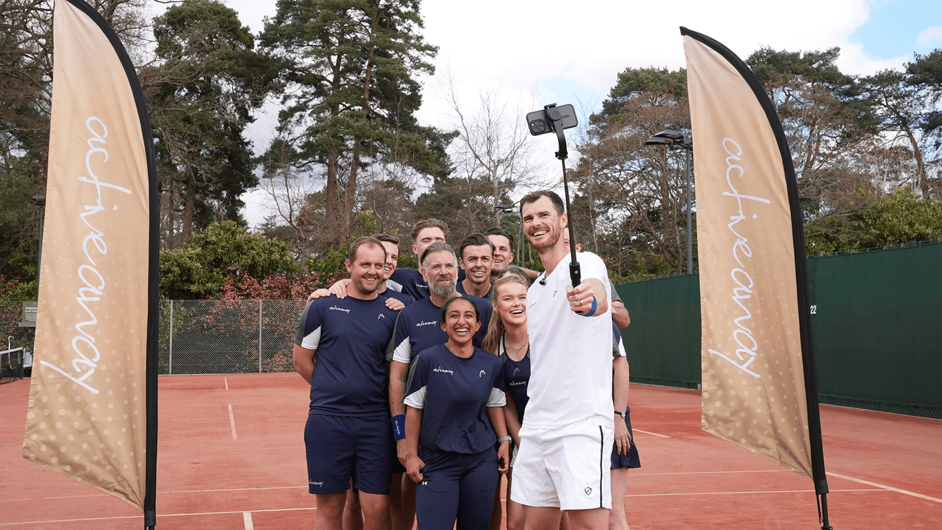 Smiling group takes a selfie on a clay tennis court at an Active Away coaching day.