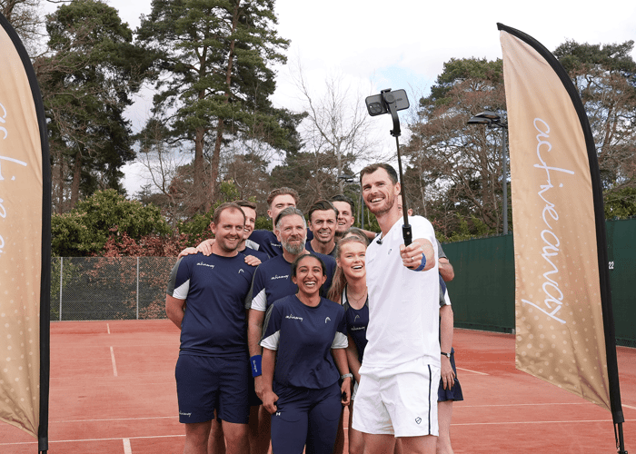 Smiling group takes a selfie on a clay tennis court at an Active Away coaching day.