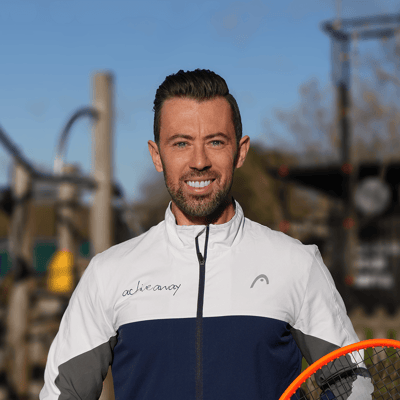Portrait of a tennis coach in an Active Away jacket holding a racket on court.