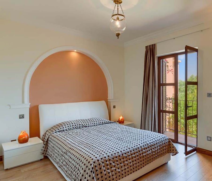 Bedroom with a double bed featuring a polka dot duvet, warm lighting, bedside tables, and a window overlooking greenery, suitable for two persons.