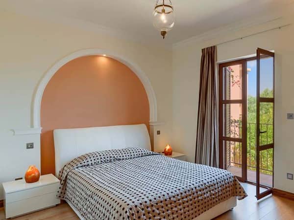 Bedroom with a double bed featuring a polka dot duvet, warm lighting, bedside tables, and a window overlooking greenery, suitable for two persons.