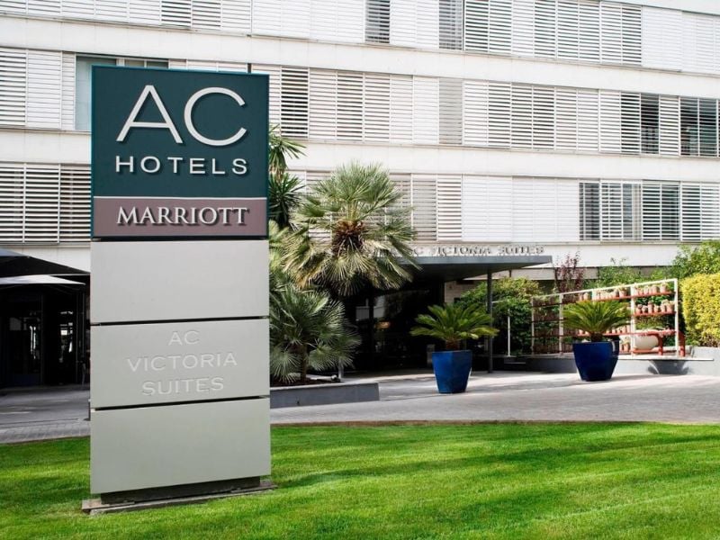Exterior of AC Hotels by Marriott with a sign reading 'AC Victoria Suites' and landscaped entrance.