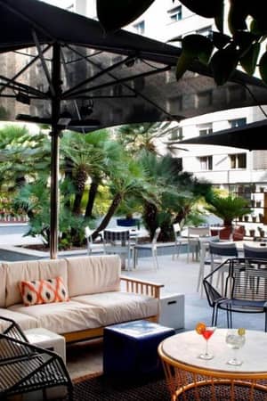 Outdoor dining area at AC Hotels with modern furniture, large umbrellas, palm trees, and a relaxed atmosphere.