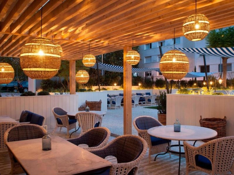 Outdoor dining area at AC Hotels with wicker furniture, marble tables, and ambient hanging lamps.