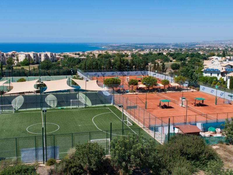 Aerial view of Aphrodite Hills sports complex featuring padel courts and football pitches with the Mediterranean Sea in the background.
