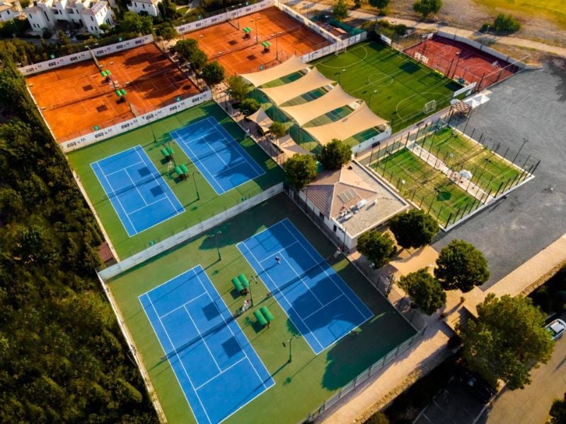 Aerial view of Aphrodite Hills sports courts including blue and green tennis courts, clay courts, and adjacent greenery.