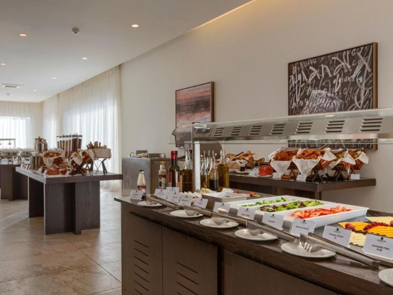 Buffet spread at Aphrodite Hills with fresh vegetables, salads, bread, condiments, oils, and modern decor in the background.