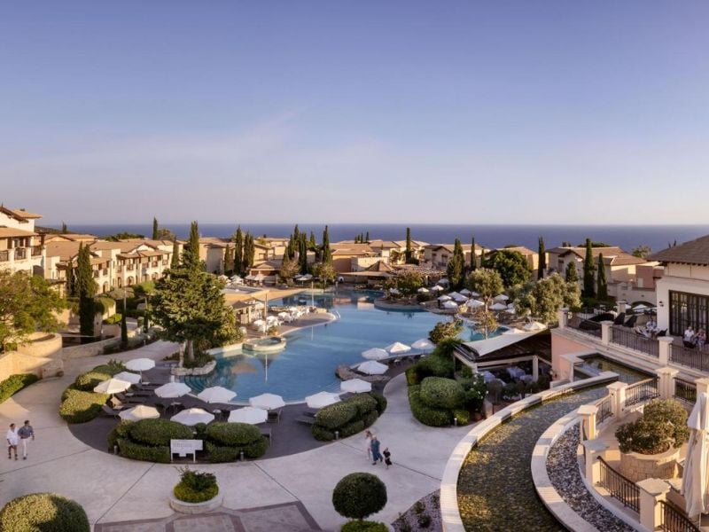 A scenic view of the Aphrodite Hills Resort pool area with umbrellas and villas, set against the Mediterranean landscape and coastline.