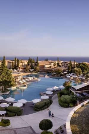 A scenic view of the Aphrodite Hills Resort pool area with umbrellas and villas, set against the Mediterranean landscape and coastline.