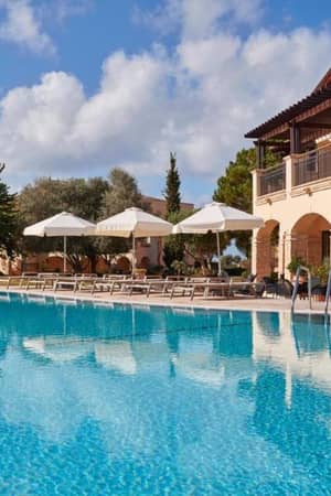 Luxury villa at Aphrodite Hills Resort with a pool, sun loungers, and white umbrellas under a clear blue sky.