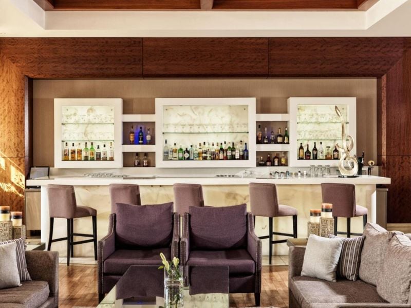 Luxurious bar at Aphrodite Hills Tennis Gallery with plush seating and shelves of premium spirits.