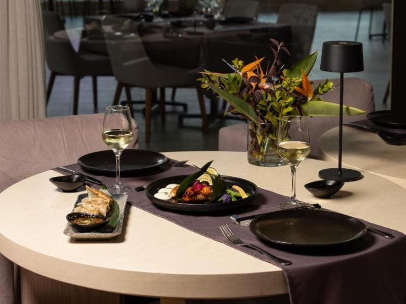 A dining table at Aphrodite Hills Tennis Gallery with elegantly presented dishes, glasses of white wine, and a floral arrangement.