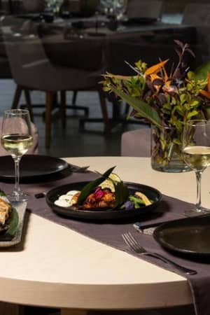 A dining table at Aphrodite Hills Tennis Gallery with elegantly presented dishes, glasses of white wine, and a floral arrangement.