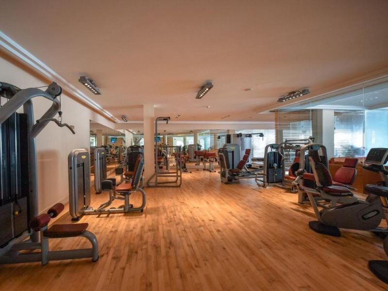 Gym interior at Aphrodite Hills Tennis Academy, equipped with weight machines and cardio stations on a wooden floor.