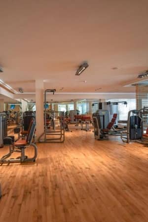 Gym interior at Aphrodite Hills Tennis Academy, equipped with weight machines and cardio stations on a wooden floor.