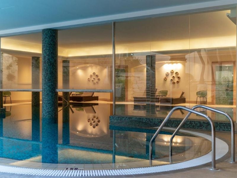 Indoor pool at Aphrodite Hills Resort with modern design, ambient lighting, and glass walls.
