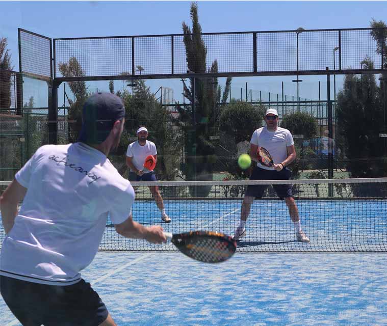 Adults playing padel on a sunlit court, engaged in a lively game with racquets in hand.