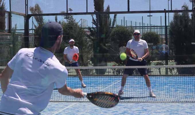 Adults playing padel on a sunlit court, engaged in a lively game with racquets in hand.