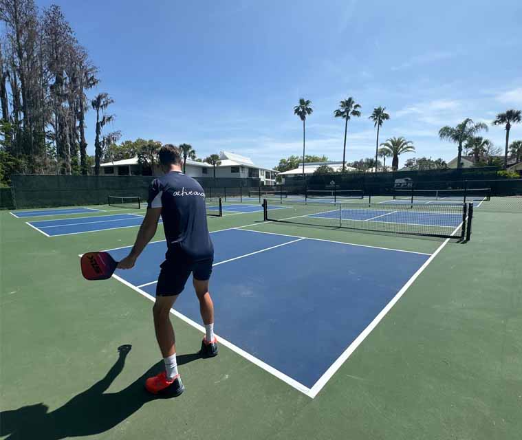 Pickleball player on a court with clear skies and lush greenery, preparing to serve during an Active Away adult holiday.