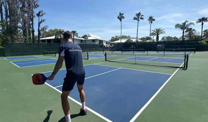 Pickleball player on a court with clear skies and lush greenery, preparing to serve during an Active Away adult holiday.