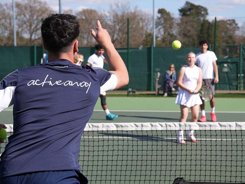 Tennis coach instructing young players on outdoor courts at Active Away Junior Tennis Camps, Royal Russell School.