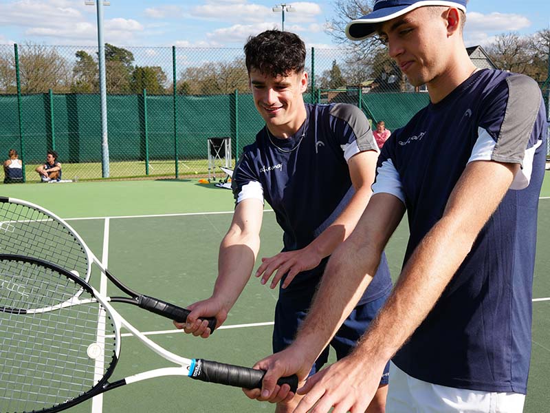 Two young male tennis players in navy sportswear holding rackets at Active Away Junior Tennis Camp, Royal Russell School tennis court.