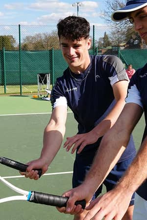 Two young male tennis players in navy sportswear holding rackets at Active Away Junior Tennis Camp, Royal Russell School tennis court.