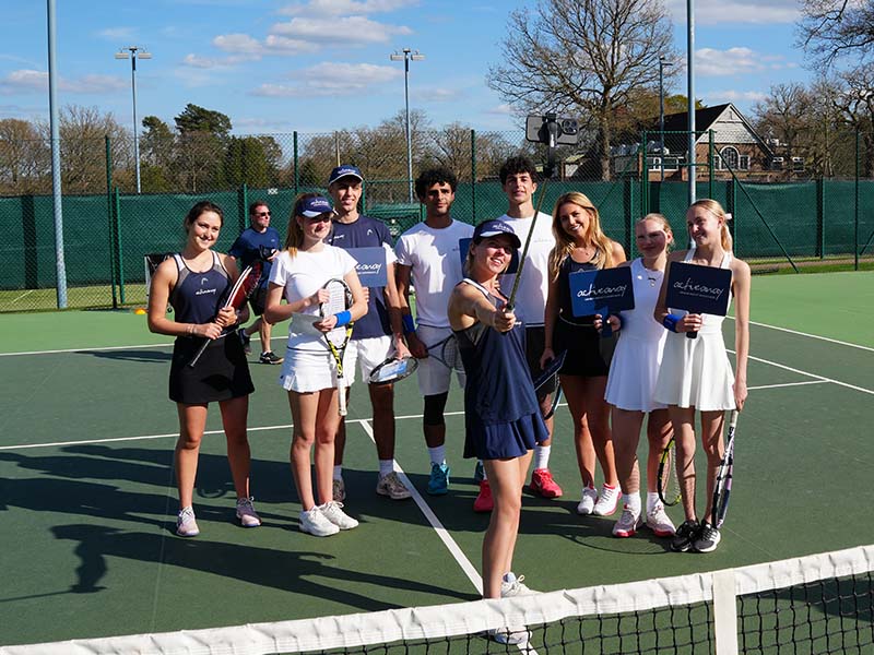 Group of junior tennis players smiling on an outdoor court at Royal Russell School during Active Away Tennis Camps.