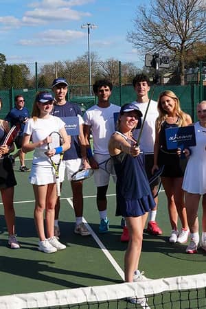 Group of junior tennis players smiling on an outdoor court at Royal Russell School during Active Away Tennis Camps.