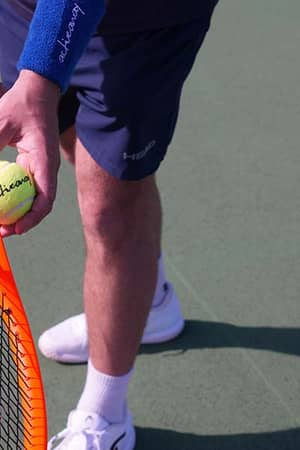 Tennis player holding a yellow tennis ball and an orange racket, ready to serve at the Active Away Junior Tennis Camps, Royal Russell School.