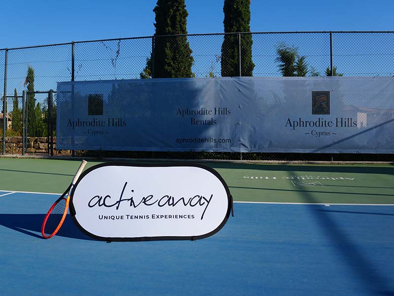 Tennis court at Aphrodite Hills Resort in Cyprus with an Active Away Unique Tennis Experiences banner.