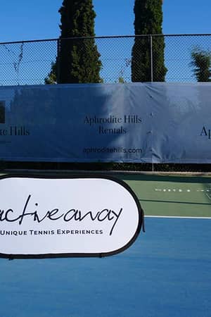 Tennis court at Aphrodite Hills Resort in Cyprus with an Active Away Unique Tennis Experiences banner.