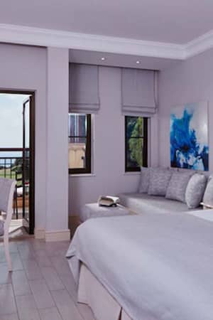 Deluxe Double Room at Aphrodite Hills with grey bedding, seating area, balcony view of greenery and sea.