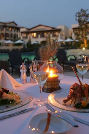 A beautifully set dining table for two with gourmet meals and a candle, overlooking a luxurious resort pool at Aphrodite Hills.
