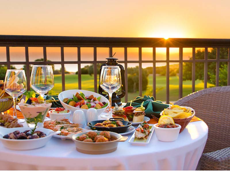Gourmet dining setup with appetisers and wine on a table overlooking a sunset at Aphrodite Hills Resort.