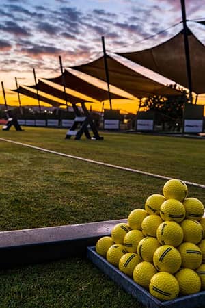 Sunset view of Aphrodite Hills driving range with stacks of yellow golf balls and canopy shades.